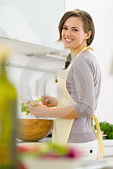 Smiling young housewife mixing salad in kitchen