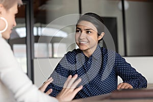 Smiling young indian businesswoman holding pleasant conversation with european colleague.