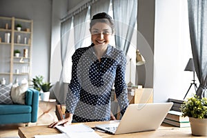 Smiling young indian woman freelancer standing at table with computer.