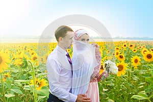 Smiling young islamic couple portrait on sunflowers field. Muslim marriage