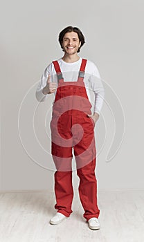 Smiling young laborer posing in work overalls and showing thumb up