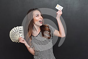 Smiling young lady holding money and debit card in hands