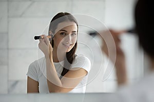 Smiling young lady standing at mirror applying flour on cheekbones