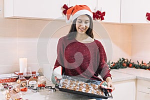 Smiling young lady wearing Christmas hat looking with satisfaction at her homemade gingerbread cookies.