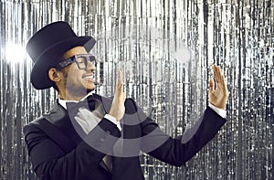 Smiling young latin american in black tuxedo holding empty space on shiny silver background.