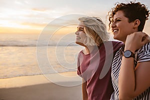 Smiling lesbian couple watching the sunset together at a beach