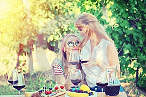 Smiling young lesbian couple women sitting affectionately together outdoors drinking red wine while bonding