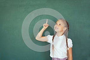 Smiling young little child girl in school on blackboard background. Education and school concept