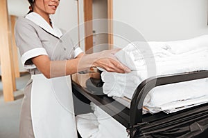 Smiling young maid taking fresh towels from a housekeeping cart