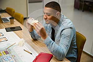 Smiling young male architect sitting and looking at building model