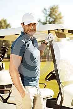 Smiling young male golfer standing at the golf cart