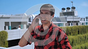 Smiling young male talking cellphone outside on the roof. Portrait of ambitious business man talking mobile phone