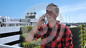 Smiling young male talking cellphone outside on the roof. Portrait of ambitious business man talking mobile phone