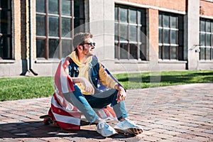 smiling young man with american flag sitting on longboard