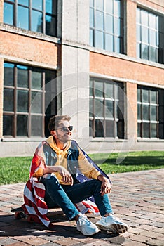 smiling young man with american flag sitting on longboard