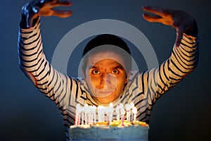 Smiling young man around while sitting in front of a cake with lit candles for his birthday