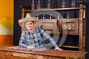 Smiling young man as bartender in a sombrero leaned on bar count