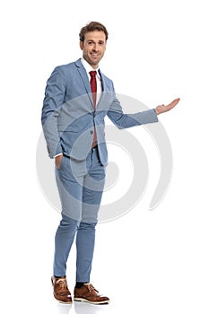 Smiling young man in blue suit presenting to side and walking