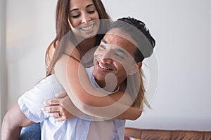 Smiling young man carrying woman on his back and laughing at home - young couple people in piggyback have fun together enjoying
