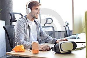 Smiling young man in casual clothing using computer, streaming playthrough or walkthrough video