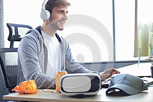 Smiling young man in casual clothing using computer, streaming playthrough or walkthrough video