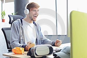 Smiling young man in casual clothing using computer, streaming playthrough or walkthrough video