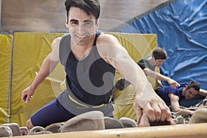 Smiling young man climbing up a climbing wall in an indoor climbing gym, directly above photo