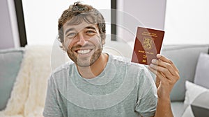 Smiling young man, confidently holding finland passport, chilling at home on the sofa, ready to embrace his upcoming travel
