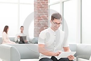 Smiling young man with digital tablet sitting in office lobby .