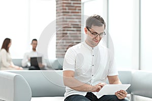 Smiling young man with digital tablet sitting in office lobby .