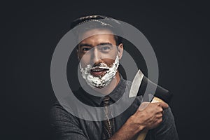 Smiling young man in flat cap and with shaving cream on his face, grooming his beard