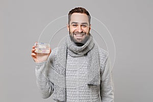 Smiling young man in gray sweater, scarf isolated on grey background, studio portrait. Healthy lifestyle, ill sick