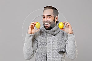 Smiling young man in gray sweater, scarf posing isolated on grey wall background, studio portrait. Healthy fashion