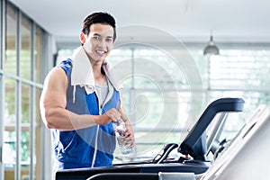 Smiling young man on treadmill holding water bottle