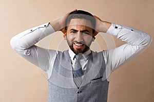 Smiling young man with hands behind head against beige background