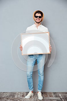 Smiling young man in hat and sunglasses holding white board