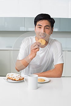 Smiling young man having biscuits and coffee in kitchen