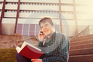 Smiling young man holding book and speaking on mobile phone in a