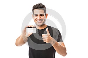 Smiling Young Man Holding Credit Card While Gesturing Thumbs Up