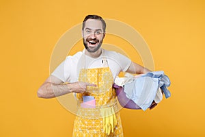 Smiling young man househusband in apron doing housework isolated on yellow background studio portrait. Housekeeping