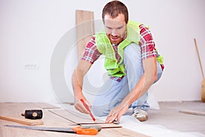 Smiling young man installing laminate flooring in new apartment