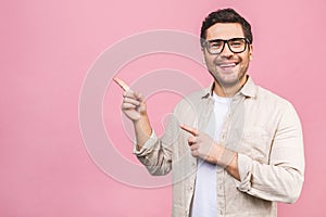 Smiling young man isolated on pink background. Stylish man wearing glasses, looking at camera and pointing finger