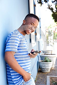Smiling young man leaning against wall and holding cellphone