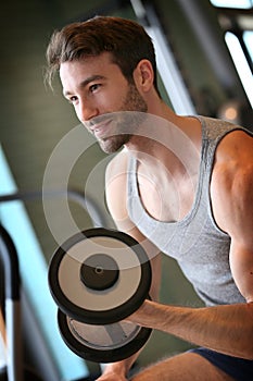 Smiling young man lifting weights in a fitness club