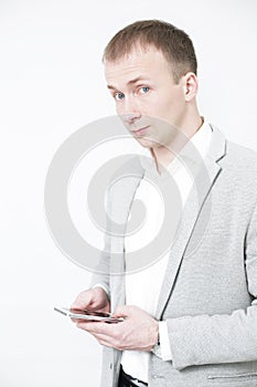 Smiling young man looking at his smart phone while text messaging on white background.