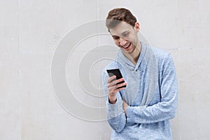 Smiling young man looking at mobile phone by wall