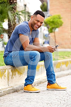 Smiling young man with mobile phone sitting on sidewalk