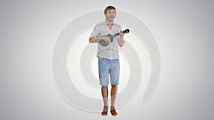 Smiling young man playing ukulele and singing looking into the c