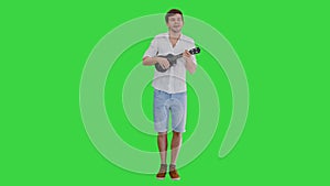 Smiling young man playing ukulele and singing looking into the camera on a Green Screen, Chroma Key.