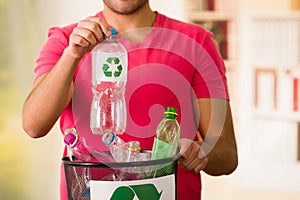 Smiling young man putting a plastic bottle inside of a small black garbage collector full of plastic, recycle and safe